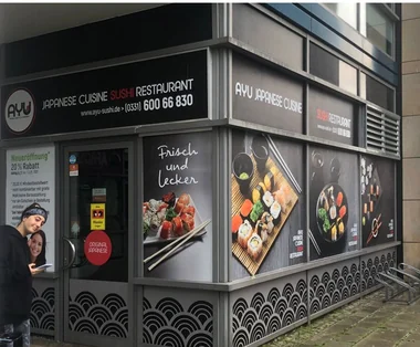 Die Filiale von Ayu Sushi in Potsdam von aussen, die Schaufenster tragen Speisenfotos und die Telefonnummer